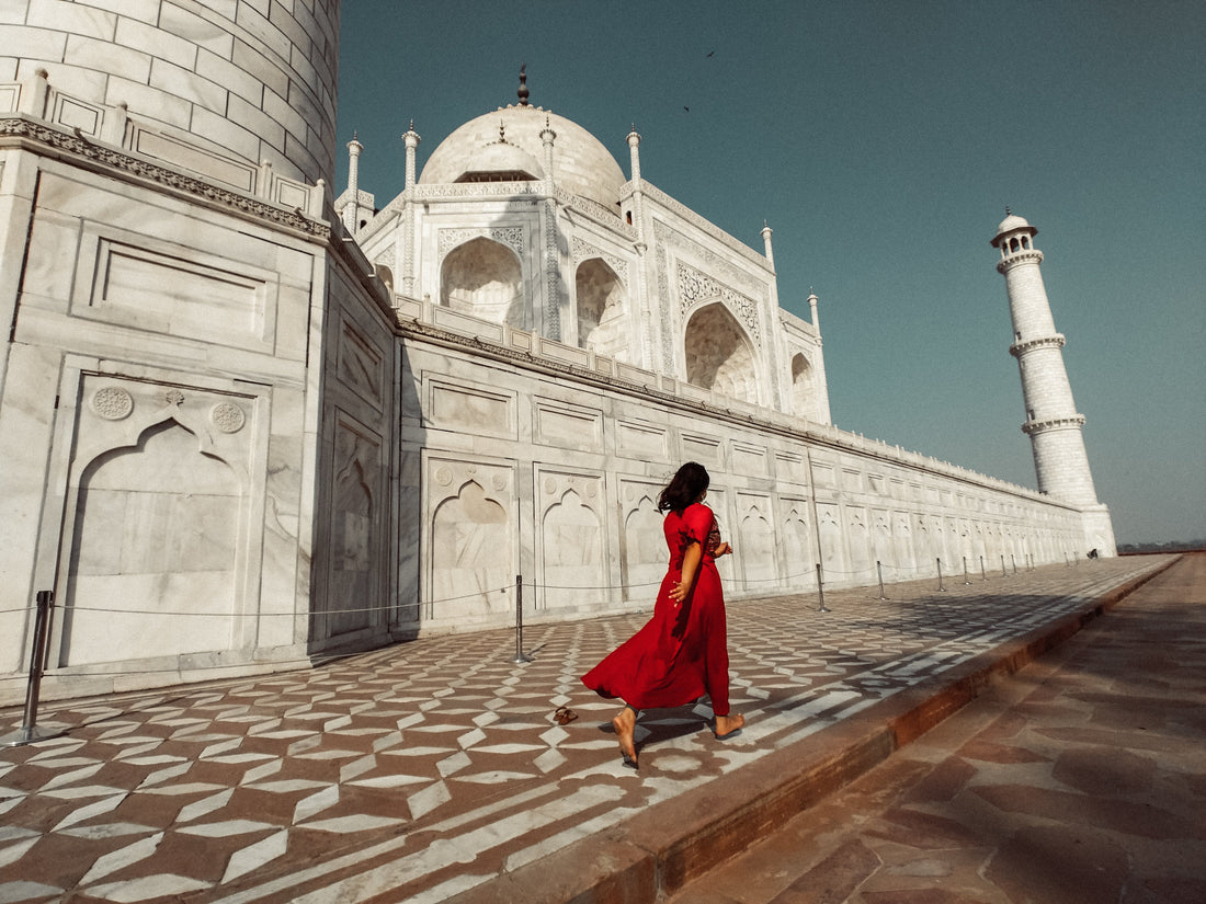 A woman in a flowing red dress walking past the Taj Mahal
