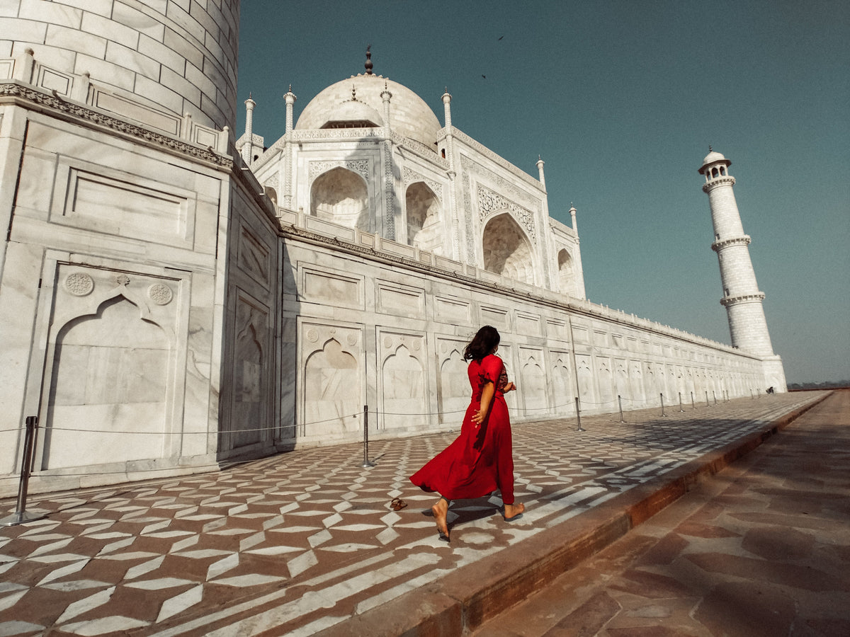 A woman in a flowing red dress walking past the Taj Mahal